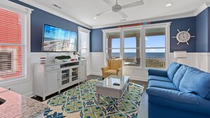 A living room with a blue couch, a glass coffee table, a TV, and a view of the ocean. - "Coral Relief" 6 Bedroom, 6.5 Bathrooms, Private Pool and Elevator! (Supply)