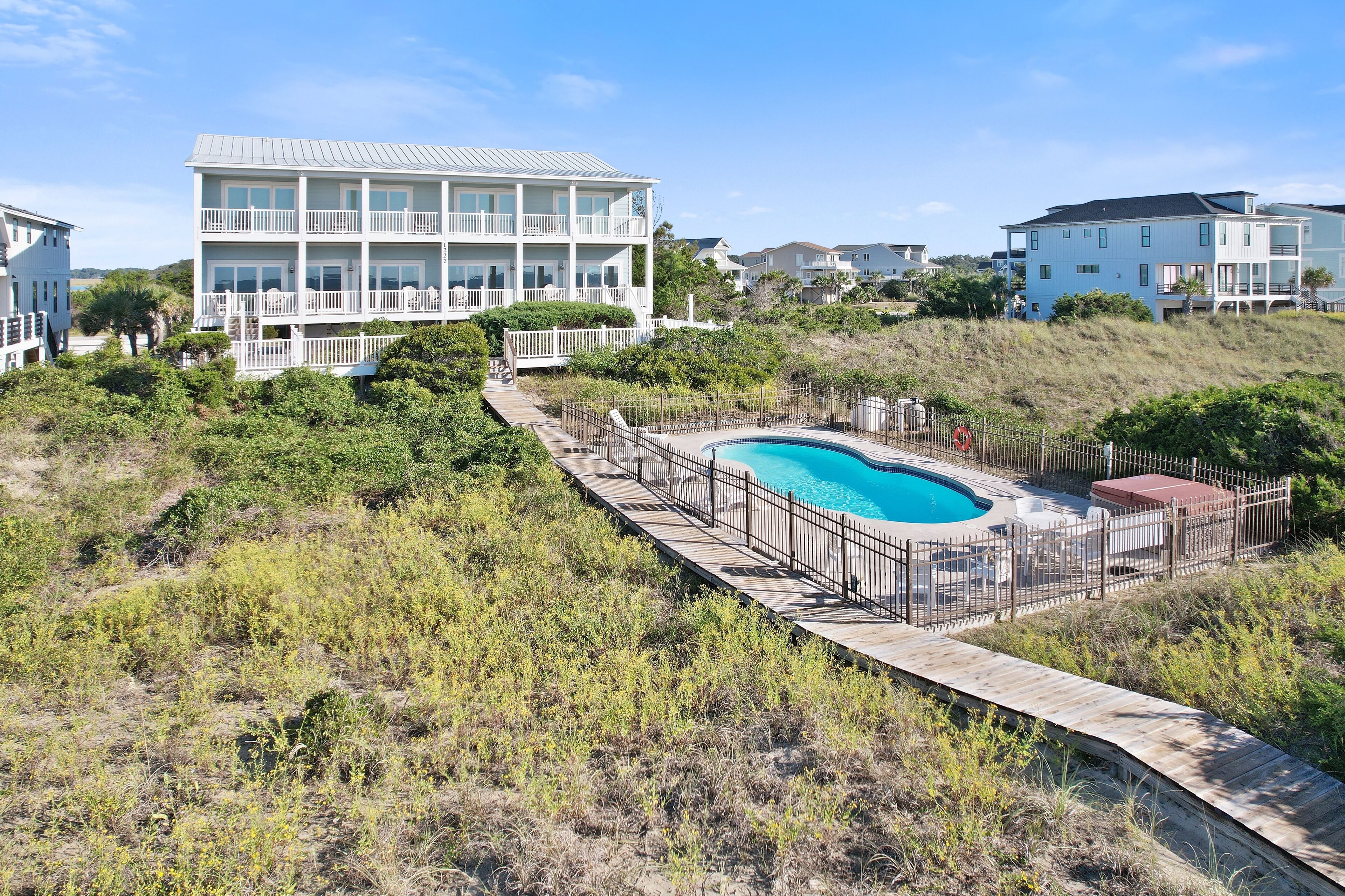 A two-story beachfront house with a swimming pool and a wooden deck.