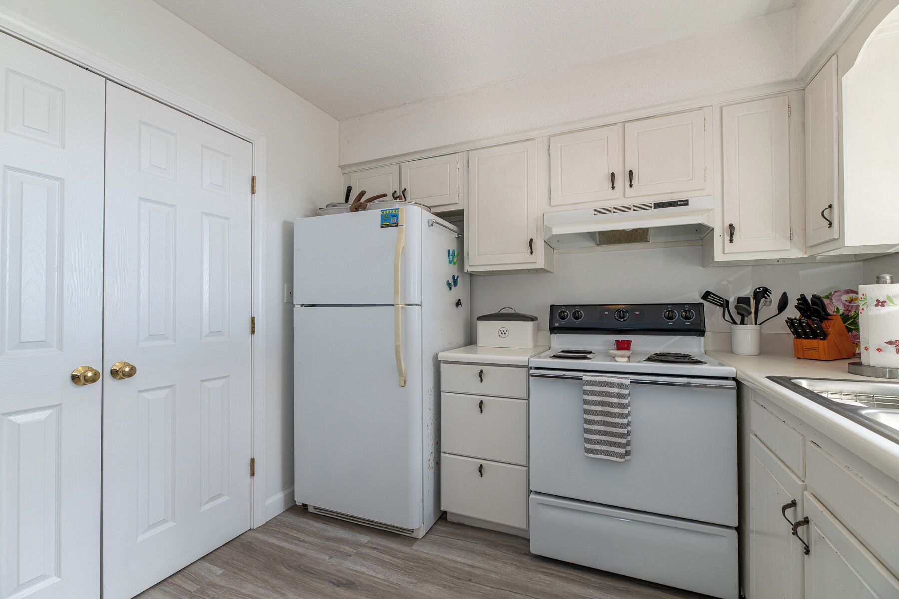 A compact kitchen with white cabinetry, a refrigerator, a stove, and a sink.