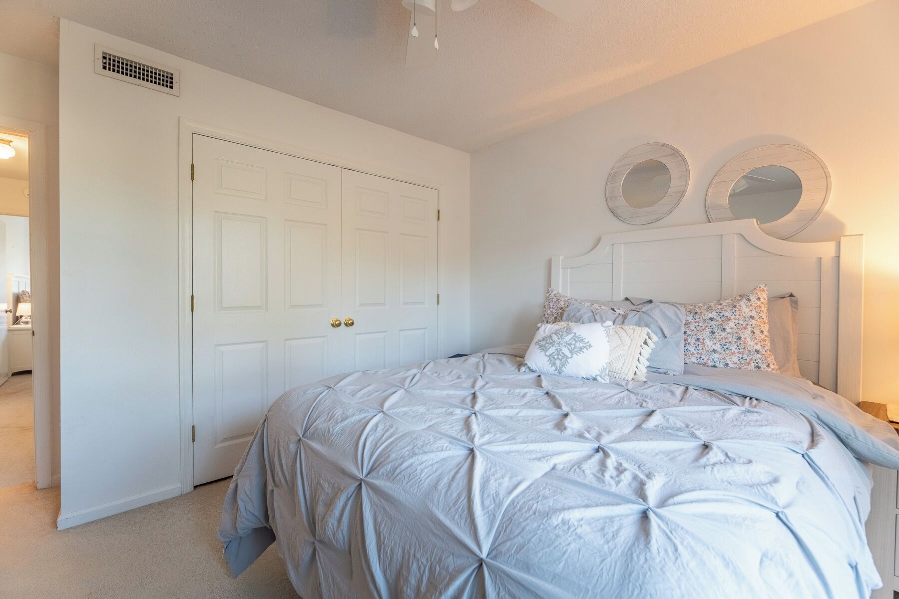 A bedroom with a large bed, a white door, and two wall-mounted mirrors.