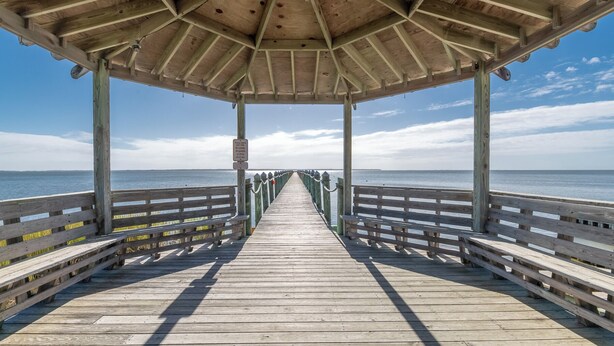 Un muelle de madera que conduce a un área techada con vista despejada al mar.