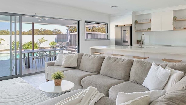Un salon moderne avec un grand canapé, une table basse et un coin repas avec des chaises. Une porte-fenêtre coulissante donne accès à un balcon aménagé avec du mobilier d’extérieur.