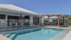 Un espace piscine moderne avec une eau d’un bleu limpide, entouré d’une terrasse couverte aménagée avec des sièges.