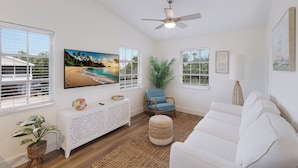 A living room with a white sofa, a blue armchair, a white console table, a large TV, and a ceiling fan.