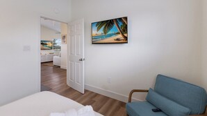 A bedroom with a bed, a blue chair, and a painting of a beach scene.