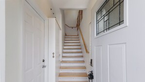A narrow hallway with white doors, a wooden staircase, and a window with a metal grill.
