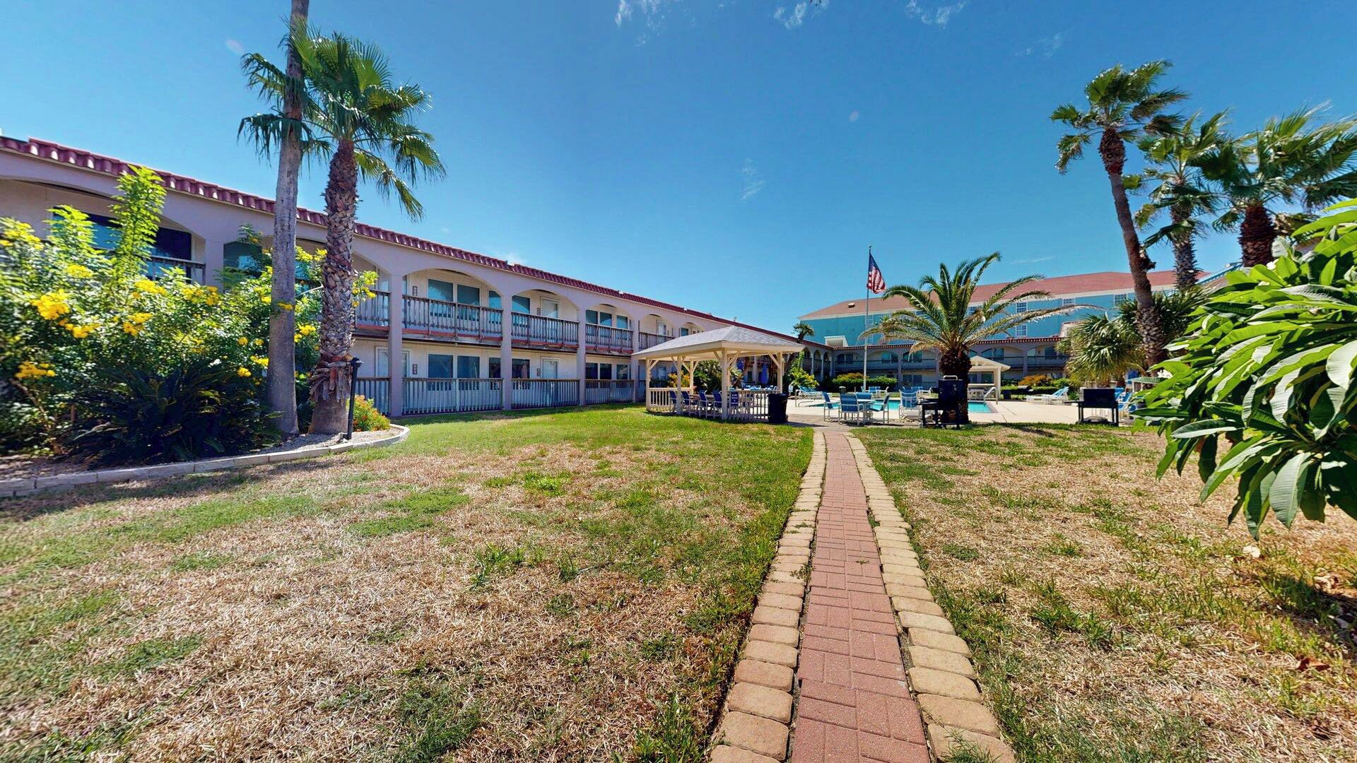 A hotel with a covered outdoor area, a pool, and palm trees.