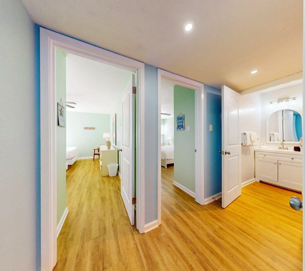 A hotel room with a wooden floor, a bed, a desk, and a bathroom with a sink and mirror.