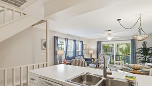 Una cocina moderna con un lavamanos doble, armarios blancos y una zona de comedor con mesa y sillas.