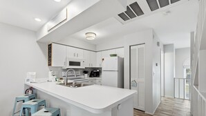 Una cocina moderna con armarios blancos, una isla central con taburetes, un microondas, un refrigerador y un lavamanos.