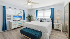 Un dormitorio con cama, televisor, ventilador de techo y ventana con cortinas.