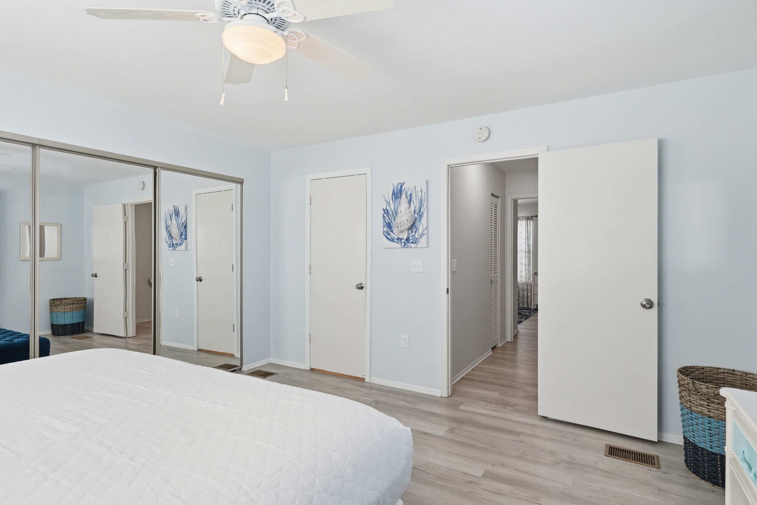 A bedroom with a bed, a ceiling fan, and a hallway leading to another room.