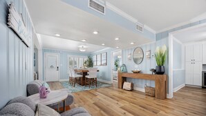 A spacious living area with a wooden floor, a dining table with chairs, a sofa, and a fireplace. - The High Tide Hideaway @ The Beach  (North Myrtle Beach)