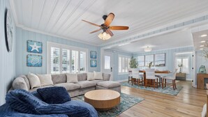 A spacious living room with a sectional sofa, a round coffee table, and a dining area with a wooden table and chairs. - The High Tide Hideaway @ The Beach  (North Myrtle Beach)