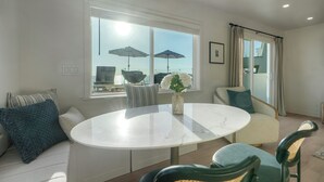 Un espace repas moderne avec une table ronde, deux chaises, un vase de fleurs et une vue sur la ville grâce à de grandes fenêtres.