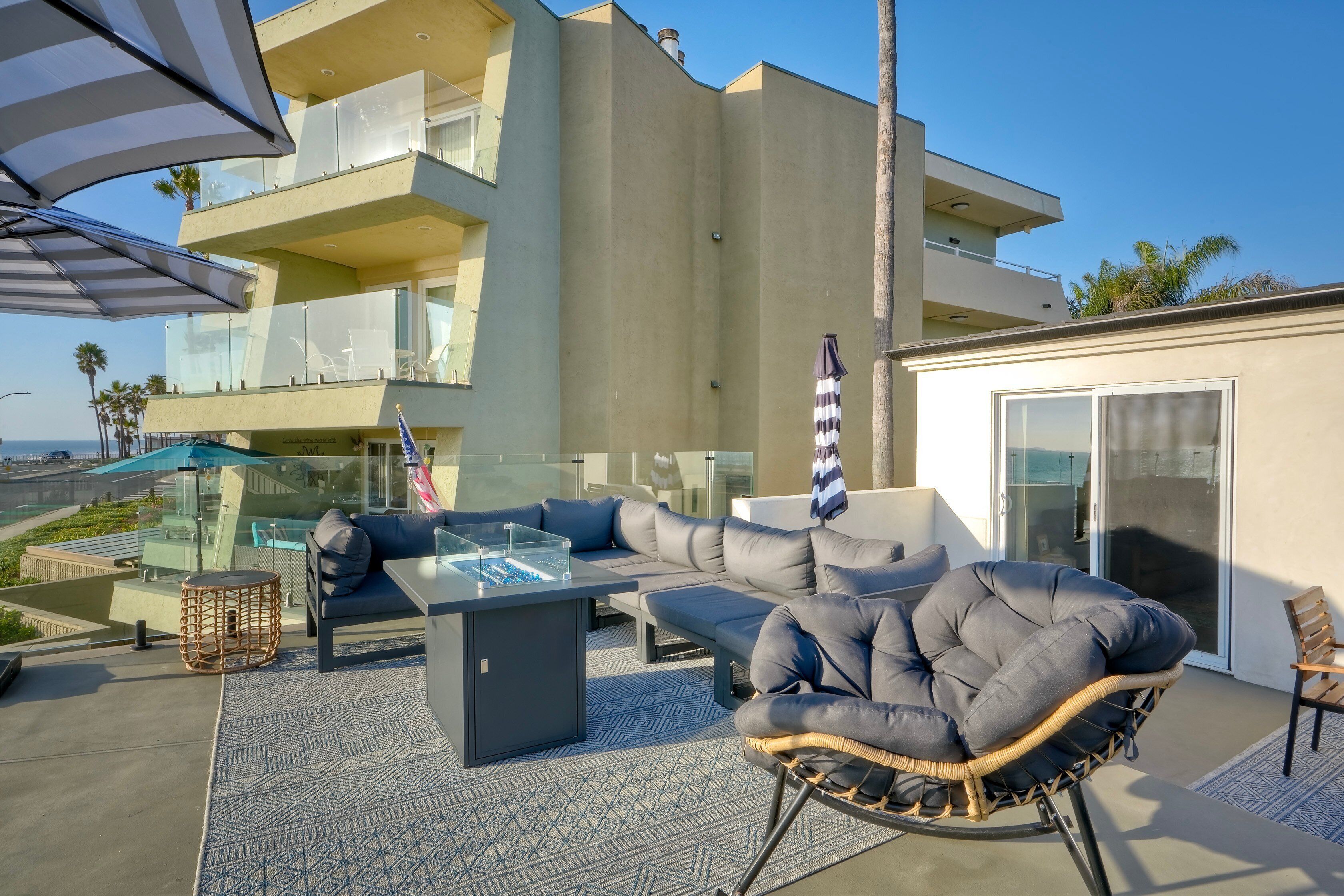 A modern outdoor seating area with a glass-top table, cushioned chairs, and a wicker chair.