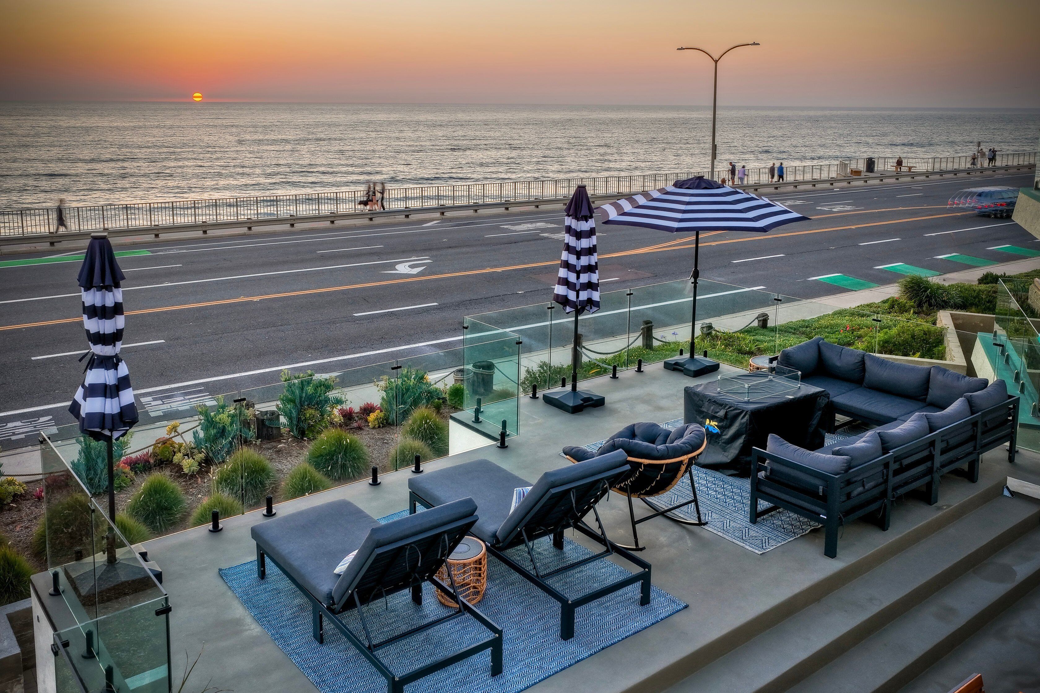 Une terrasse sur le toit avec des sièges extérieurs, une vue sur le coucher de soleil sur l’océan et une rue en arrière-plan.