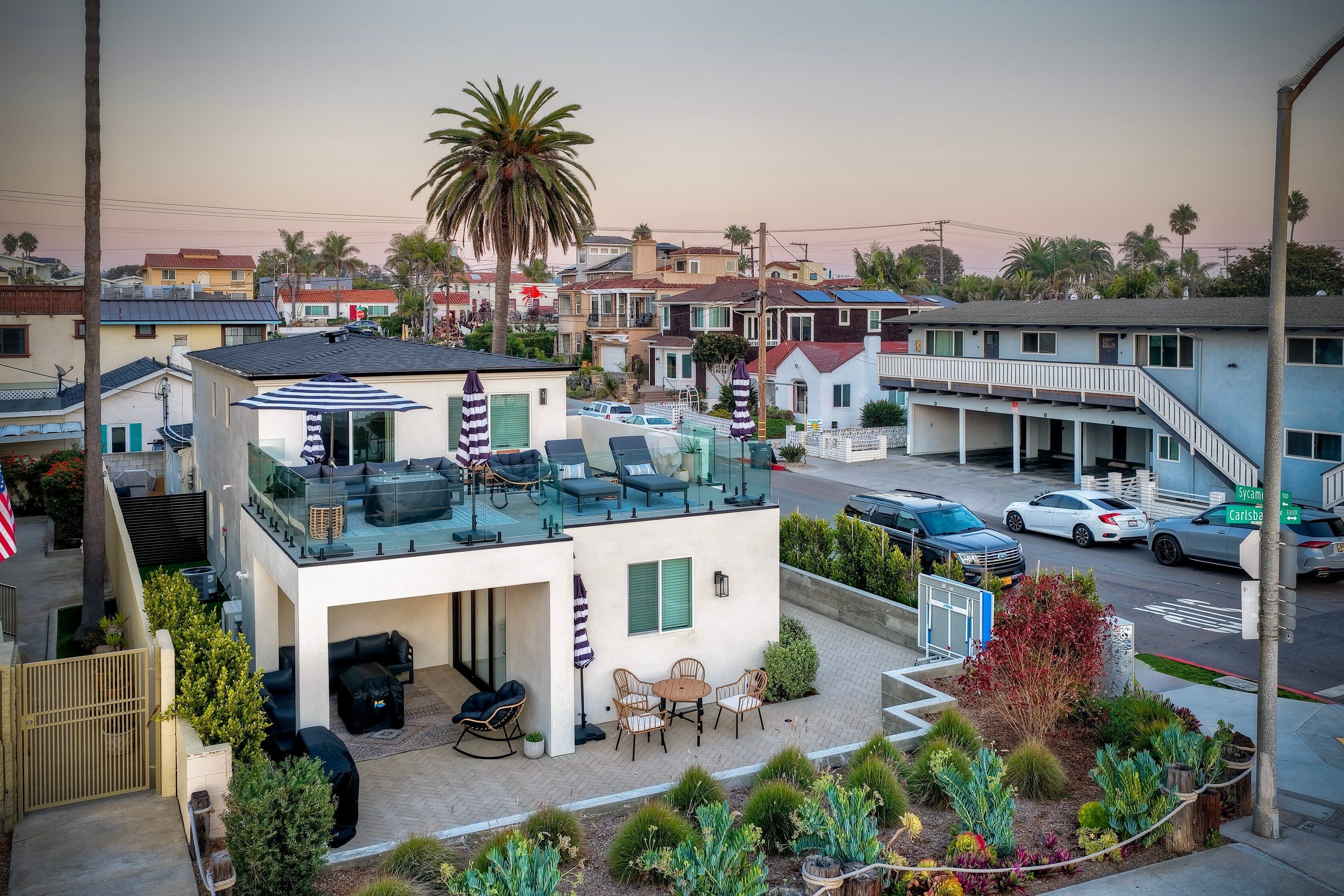 A modern two-story house with a glass balcony, outdoor seating, and a well-maintained garden.