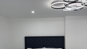 Un dormitorio moderno con una cama grande, dos mesitas de noche, un espejo redondo y un aplique de techo.