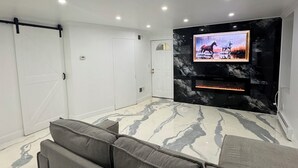 Una sala moderna con un televisor de pantalla plana grande montado en una pared de mármol, iluminación empotrada en el techo y un sofá modular gris.