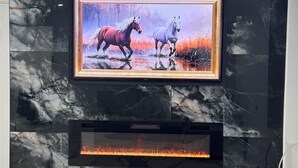 Una sala de estar moderna con una pared de mármol, un cuadro enmarcado de caballos y una chimenea empotrada.