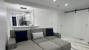Un salón moderno con un sofá seccional gris, un espejo grande y un piso blanco con diseños tipo mármol.