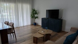 A living room with a dining table, chairs, a sofa, a TV stand, and a potted plant. - Tracadero Lodge H2 Apt, 1 Bedroom (Dominicus)
