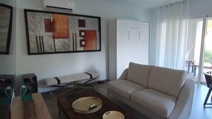 A modern living room with a sofa, coffee table, artwork, and a ceiling fan. - Tracadero Lodge A1, 1 Bedroom (Dominicus)