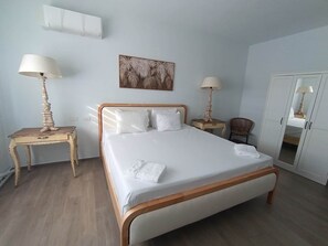 A neatly arranged bedroom with a bed, bedside tables, a chair, a wardrobe, and a wall-mounted artwork.