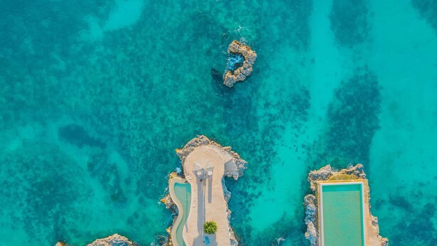 An aerial view of a coastal resort with a swimming pool, beach area, and rocky outcrops. - Tracadero Lodge A1, 1 Bedroom (Dominicus)