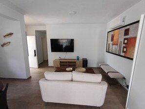 Ein modernes Wohnzimmer mit einem weißen Sofa, einem Flachbildfernseher, einer Holz-Unterhaltungseinheit und einem Gemälde an der Wand.