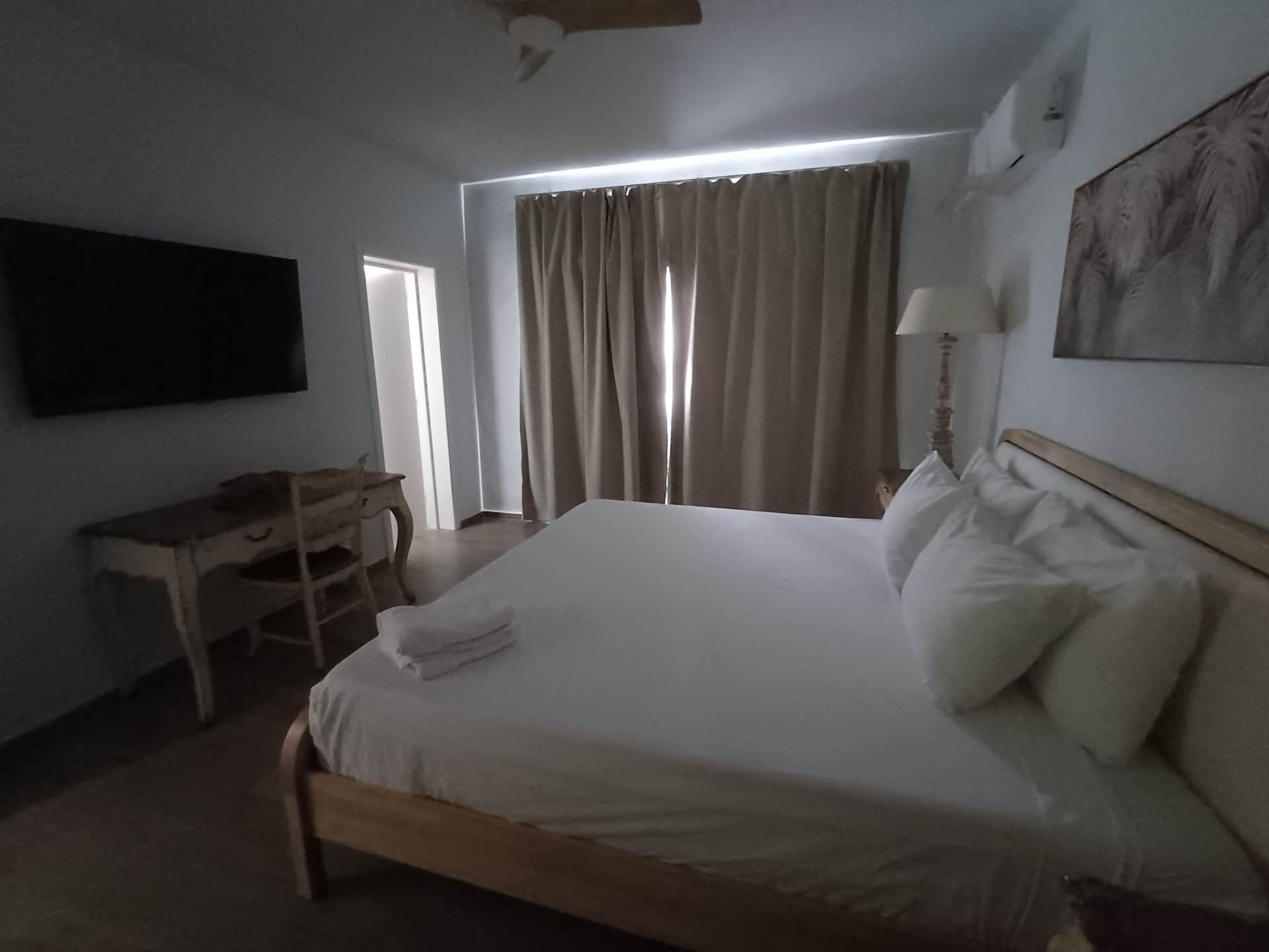 A hotel room with a bed, a desk, a television, a window with curtains, and a painting on the wall.