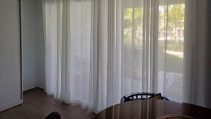A room with a wooden table, a chair, and sheer white curtains. - Tracadero Lodge A1, 1 Bedroom (Dominicus)