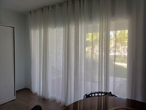 A room with a wooden table, a chair, and sheer white curtains.