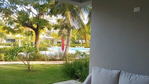 A modern living room with a white sofa, a wooden coffee table with a plant, and a view of a pool and greenery outside. - Tracadero Lodge A1, 1 Bedroom (Dominicus)