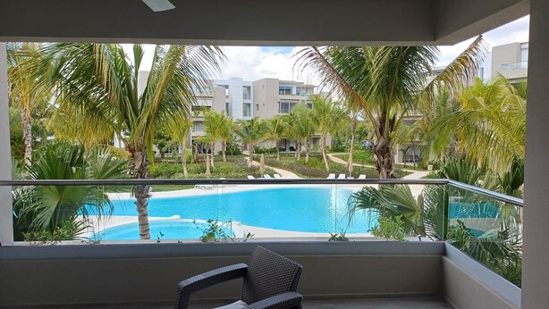 A balcony with a view of a swimming pool surrounded by palm trees and buildings. - Tracadero Lodge G3 Apt, 2 Bedroom (Dominicus)