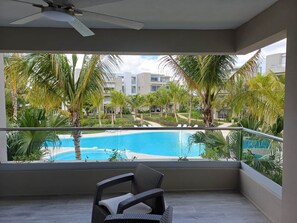 Un balcon donnant sur une piscine entourée de palmiers et de bâtiments.