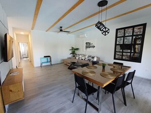 Un salon moderne avec une table à manger en bois, des chaises noires, un ventilateur de plafond et une grande fenêtre décorative.