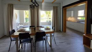 A modern dining area with a wooden table and chairs, a hanging light fixture, and a view of the outdoors. - Tracadero Lodge G3 Apt, 2 Bedroom (Dominicus)