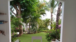A white table with four chairs in a room with a view of a garden with palm trees and a lawn. - Tracadero Marina 26 Apt, 3 Hab. (Dominicus)