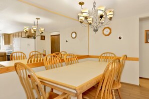 A dining area with a large table and wooden chairs, a chandelier, and a clock on the wall. - Summit Ski Resort Mountain View Condo - Walk to Snow Summit (Big Bear Lake)