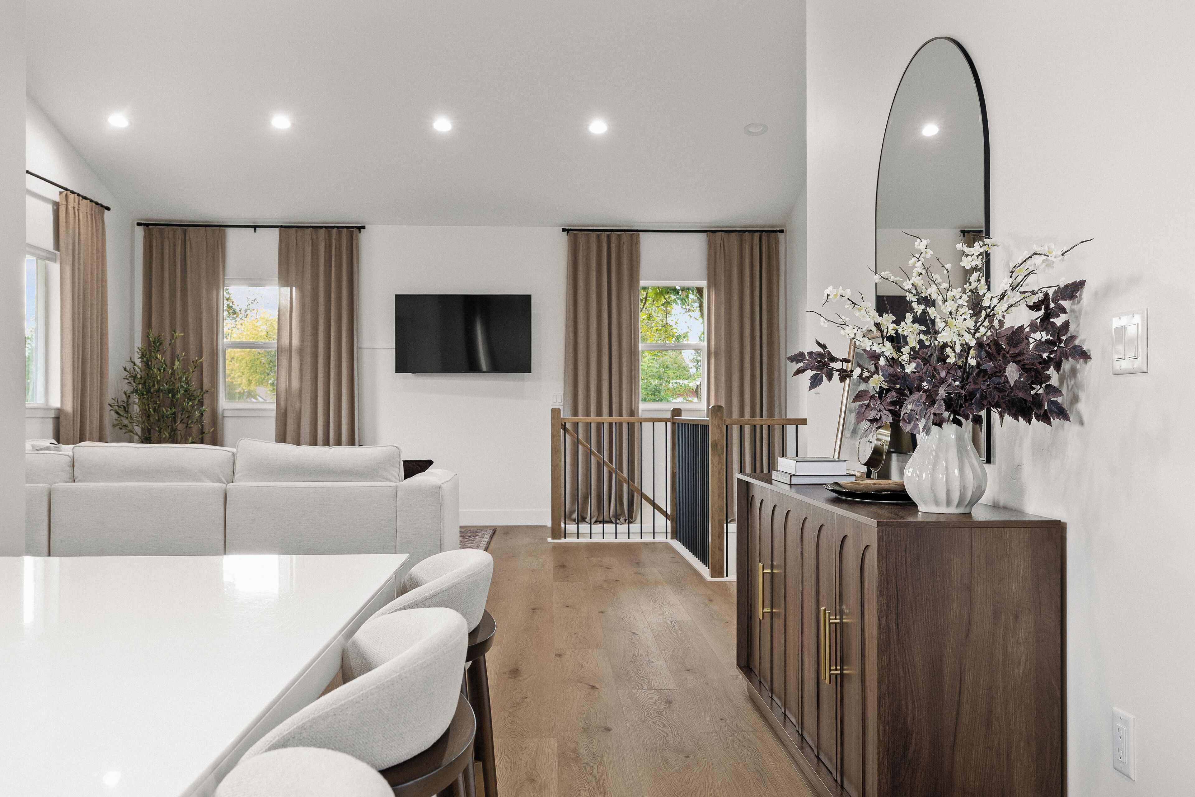 Un salon moderne avec un canapé blanc, une table à manger avec des chaises, un meuble en bois et un grand miroir au mur.