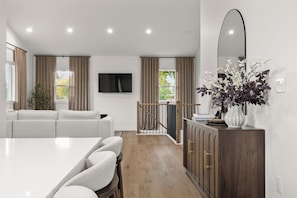 A modern living room with a white sofa, a dining table with chairs, a wooden cabinet, and a large mirror on the wall. - New! Cozy Cottage in Spokane Valley (Spokane Valley)