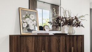 Um armário de madeira escura com puxadores dourados, um espelho em cima e uma moldura com uma imagem de flores.