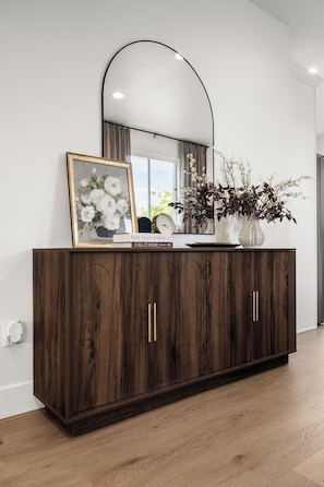 A dark wood cabinet with gold handles, a mirror above it, and a framed picture of flowers. - New! Cozy Cottage in Spokane Valley (Spokane Valley)