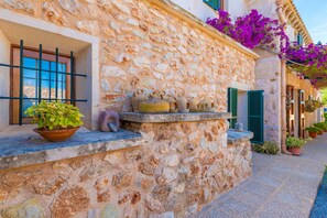 A stone building with a window, a shelf with pottery, and potted plants.