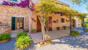 Un bâtiment en pierre doté d’une cour, de plantes en pot et d’une pergola couverte de plantes grimpantes en fleurs.