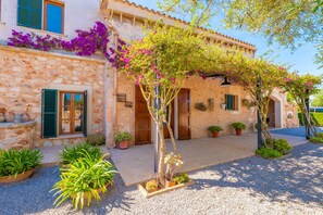 A stone building with a courtyard, potted plants, and a pergola with flowering vines.