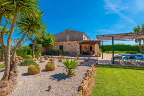 A stone house with a patio, a pool, and various cacti and plants.