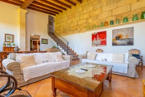 A spacious living room with a wooden staircase, two sofas, a coffee table, and a wall with art and jars.